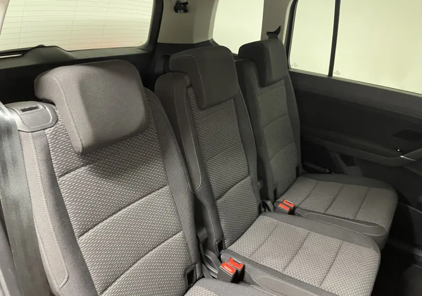 Vue intérieure sur la rangée arrière du Volkswagen Touran 2024, sièges tissu gris avec ceintures de sécurité visibles.