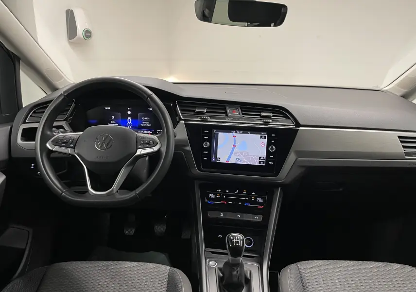 Intérieur du Volkswagen Touran 2024, vue frontale du tableau de bord avec volant, écran tactile et levier de vitesses manuel.