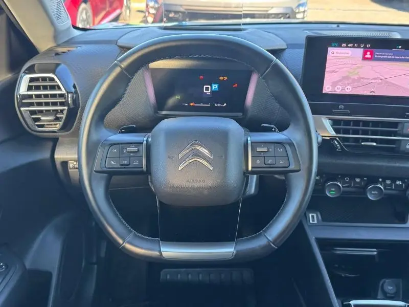 Vue centrée sur le volant cuir du Citroën C4 gris 2024, avec tableau de bord numérique et écran tactile visible.