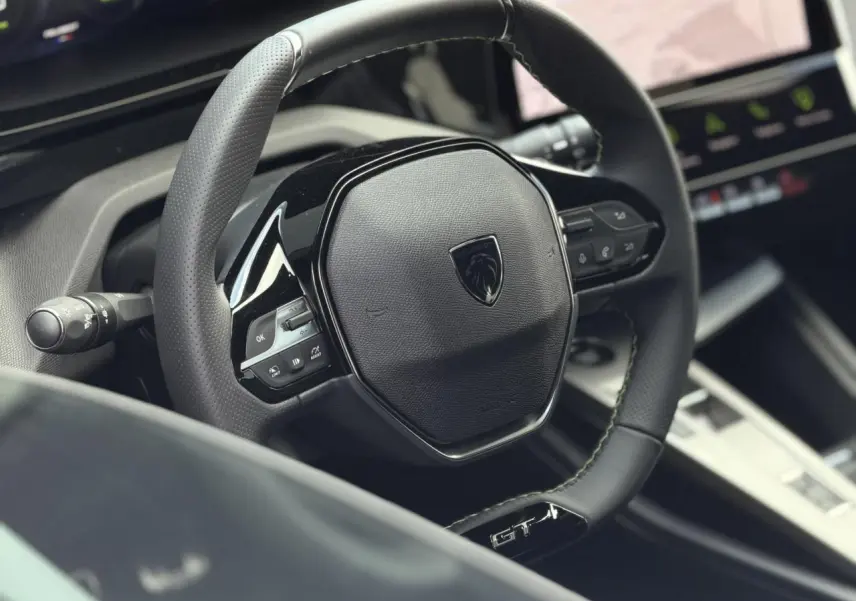 Gros plan sur le volant cuir noir GT avec surpiqûres vert Adamite de la Peugeot 308 Hybrid 2026.