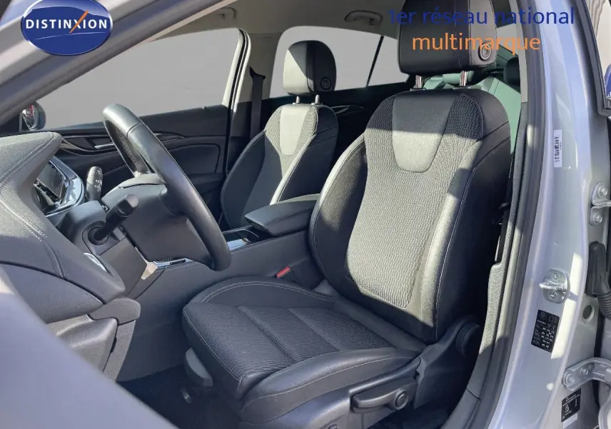 Vue intérieure côté conducteur de l'Opel Insignia 2021 avec sièges tissu noir et gris, volant et tableau de bord visibles.