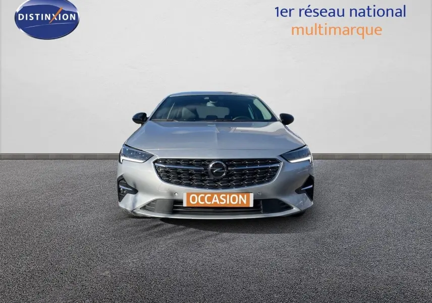 Opel Insignia gris minéral métal vue de face avec calandre noire et phares LED allumés sur fond neutre.