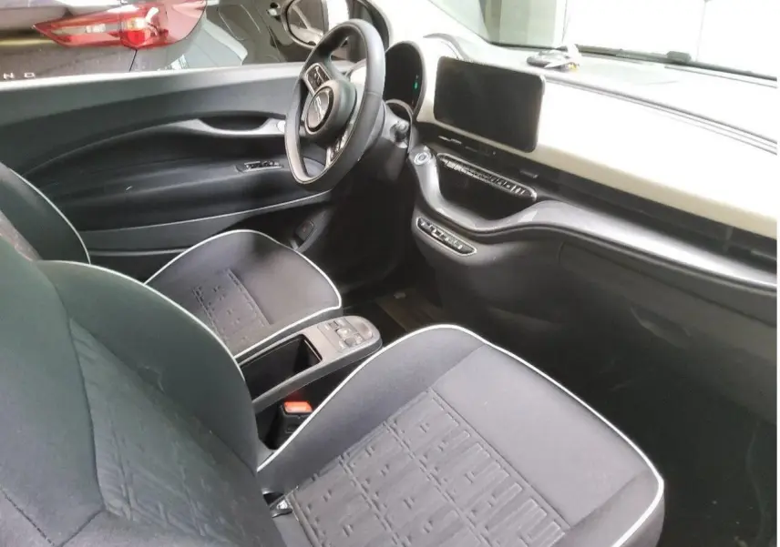 Intérieur de la Fiat 500 électrique 2024 vu côté conducteur, avec sièges noirs et tableau de bord clair épuré.