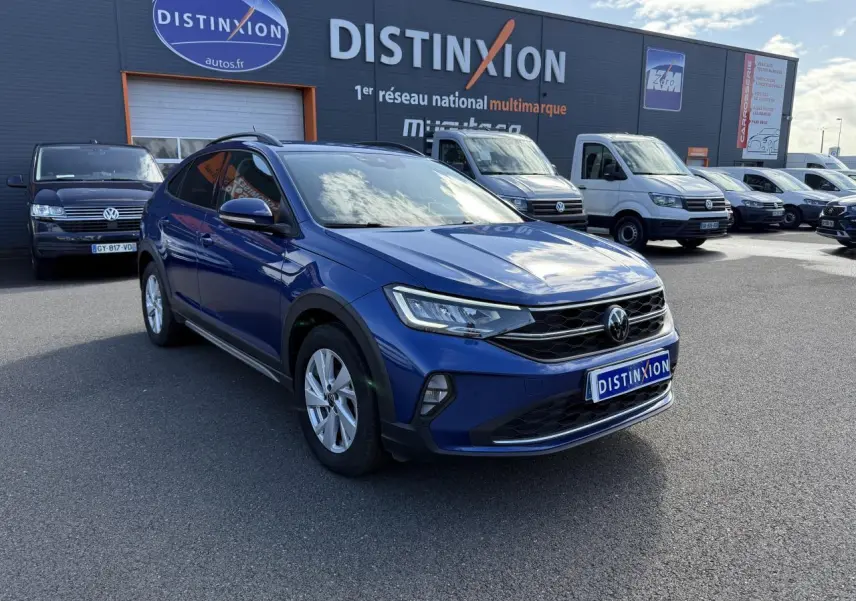 Volkswagen Taigo bleu récif métallisé en 3/4 avant droit sur parking devant concession multimarque Distinxion.