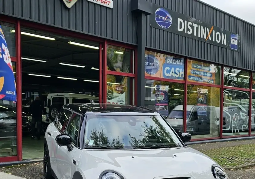 MINI Cooper S grise vue 3/4 avant droit, avec toit noir et calandre noire devant un garage auto.