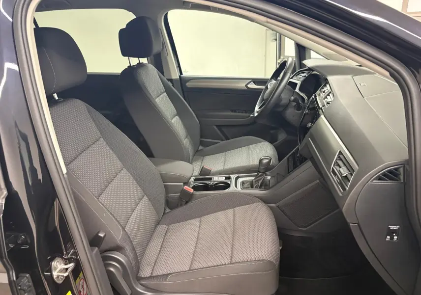 Vue intérieure côté conducteur du Volkswagen Touran 2024 noir intense nacré, montrant sièges et tableau de bord modernes.