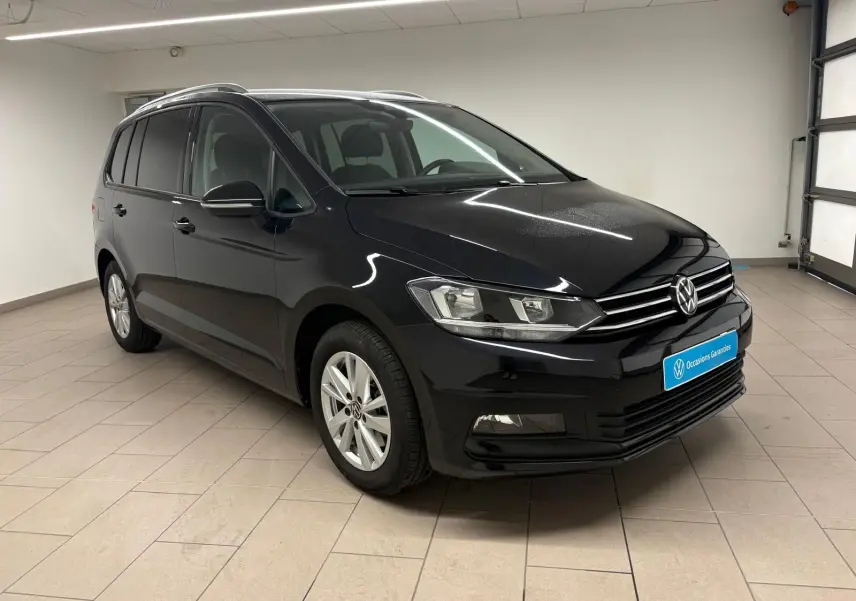 Volkswagen Touran noir intense nacré vu en 3/4 avant droit dans un garage lumineux avec jantes argentées.
