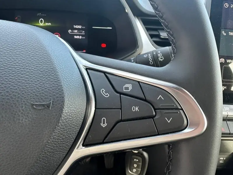 Gros plan sur les commandes multifonctions à droite du volant du Renault Captur blanc nacré 2025, avec écran et tableau de bord partiellement visibles.