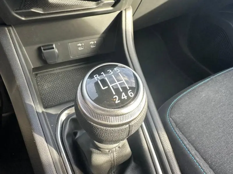 Gros plan sur le levier de vitesses manuel noir du Renault Captur 2025, avec coutures bleues visibles sur le siège tissu adjacent.