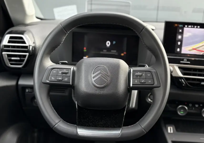 Vue rapprochée du volant cuir noir de la Citroën C4 Hybrid 2025 avec commandes intégrées et tableau de bord numérique.