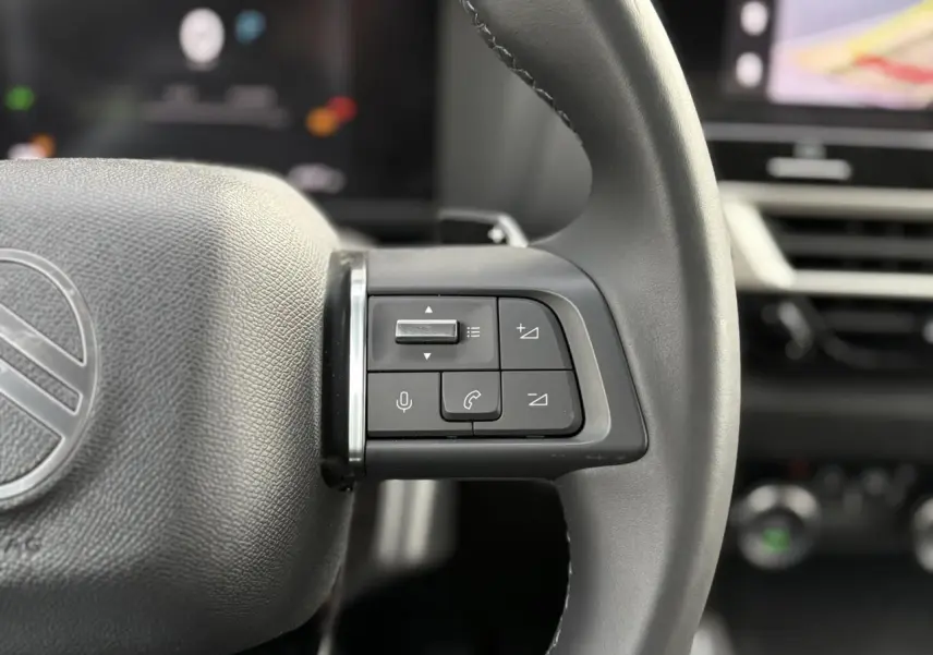 Gros plan sur les commandes à droite du volant cuir gris du Citroën C4 Hybrid 2025, avec tableau de bord flou en arrière-plan.