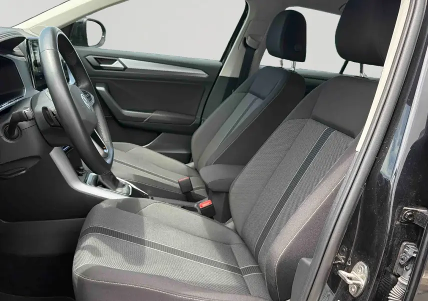 Vue intérieure côté gauche du Volkswagen T-Roc noir 2025, montrant les sièges avant en tissu gris et la console centrale.