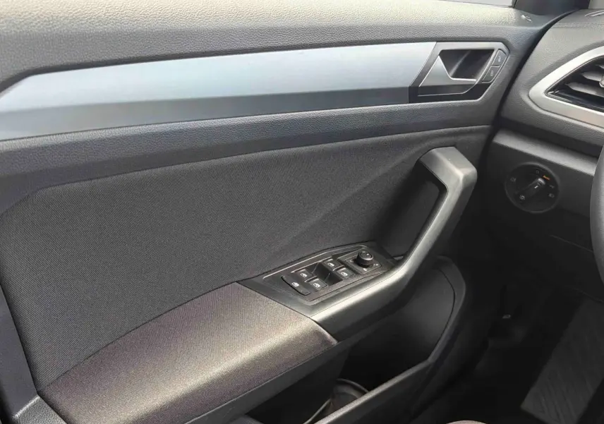 Vue intérieure côté conducteur du panneau de porte noir du Volkswagen T-Roc 2025 avec commandes électriques des vitres et rétroviseurs.