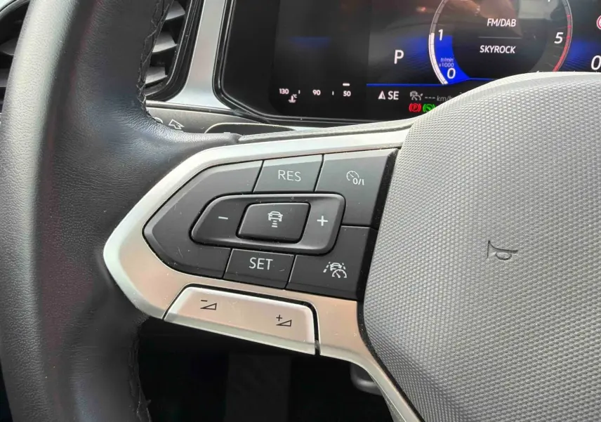 Gros plan sur le volant cuir multifonctions côté gauche du Volkswagen T-Roc noir, avec commandes de régulateur de vitesse.