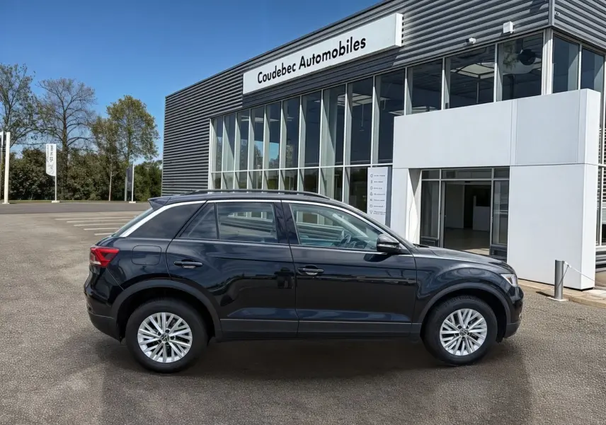 Vue de profil côté gauche d'un Volkswagen T-Roc noir stationné devant un bâtiment commercial.