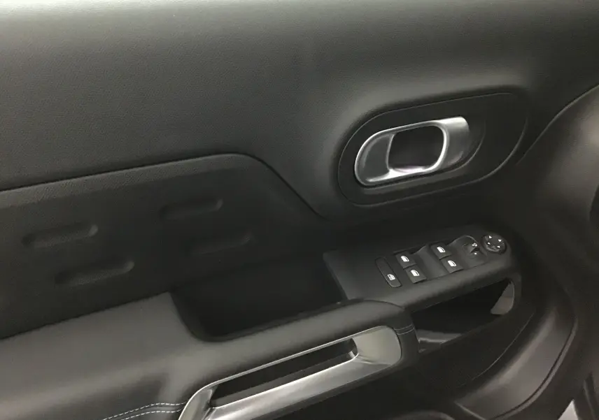 Poignée intérieure et commandes de lève-vitres côté gauche en plastique noir et métal dans un Citroën C5 Aircross 2024 gris artense.