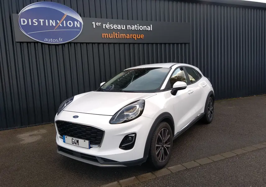 Ford Puma blanc en 3/4 avant droit, avec calandre noire et jantes foncées, stationné devant un mur gris.