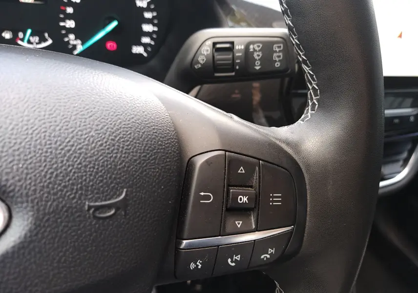 Gros plan sur les commandes au volant en cuir noir avec surpiqûres blanches du Ford Puma blanc 2021, version Titanium.