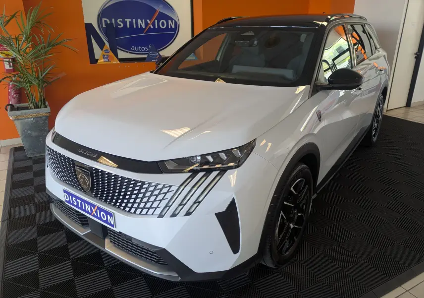 Peugeot 5008 Hybrid 145 GT blanc Okenite avec toit noir, vue 3/4 avant droit en intérieur showroom.