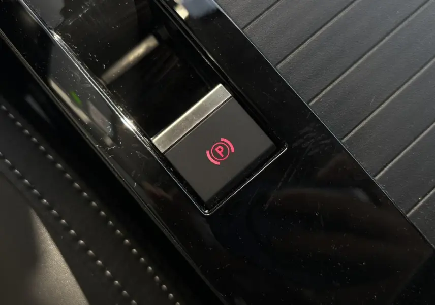 Gros plan sur le bouton de frein de stationnement électrique rouge sur console noire brillante de Citroën C4 Hybrid 2025.