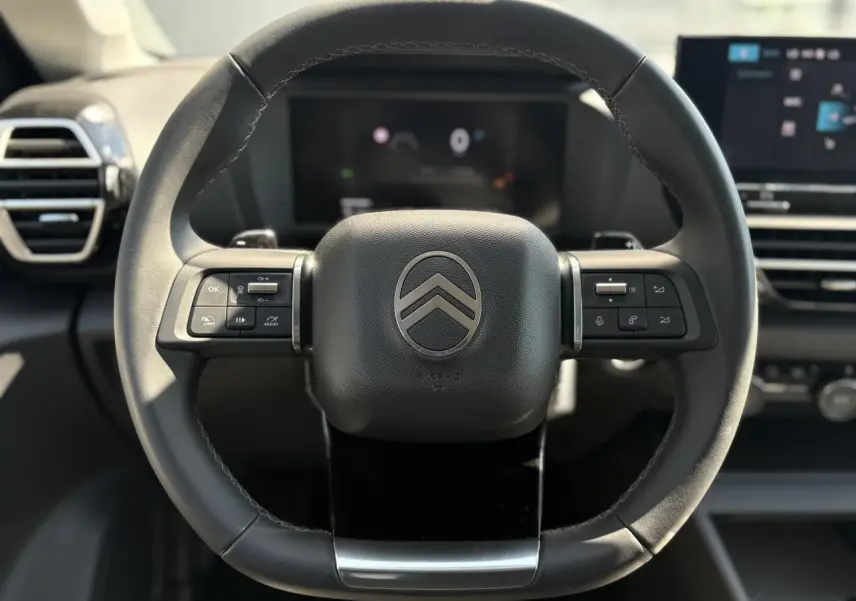 Vue rapprochée du volant cuir noir de la Citroën C4 Hybrid 2025 avec commandes intégrées et tableau de bord numérique flou.
