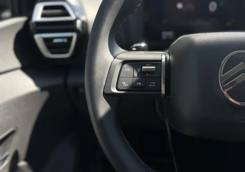 Gros plan sur la partie gauche du volant noir de la Citroën C4 Hybrid 2025 avec commandes intégrées et aérateur en arrière-plan.