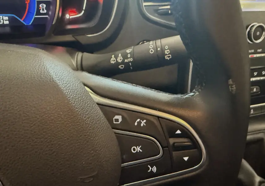 Gros plan sur le volant noir du Renault Grand Scenic IV Business avec commandes intégrées et tableau de bord partiellement visible.