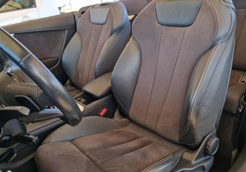 Gros plan sur les sièges avant en cuir noir de l'Audi A5 Cabriolet 2.0 TDI 190CH, avec logo S embossé sur les appuie-têtes.
