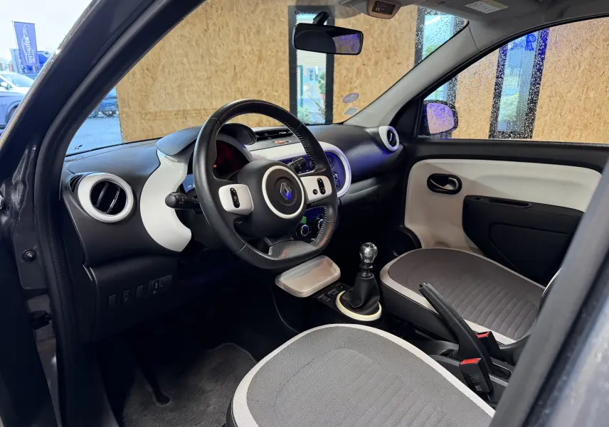 Vue intérieure côté conducteur de la Renault Twingo III gris, volant cuir multifonction et levier de vitesse manuel visibles.