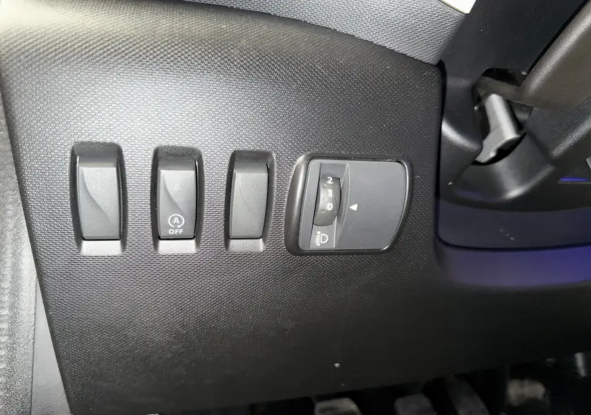Gros plan sur les commandes de réglage des phares et désactivation du start-stop dans l’habitacle d’une Renault Twingo III gris 2018.