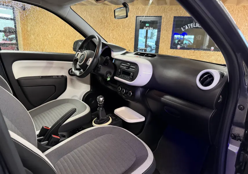 Intérieur avant droit de la Renault Twingo III gris, montrant le volant cuir, tableau de bord bicolore et boîte manuelle.