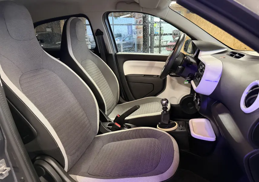 Vue intérieure côté conducteur de la Renault Twingo III gris 2018, montrant les sièges, volant cuir et levier de vitesse manuel.