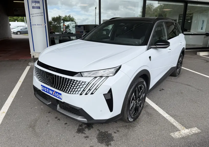 Peugeot 5008 HYBRID 145 e-DCS6 GT blanc Okenite avec toit noir, vue 3/4 avant droit sur parking devant vitrine.