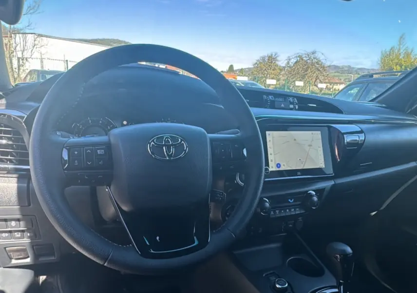 Vue intérieure centrée sur le volant cuir multifonctions et l'écran tactile du tableau de bord du Toyota Hilux 2026.