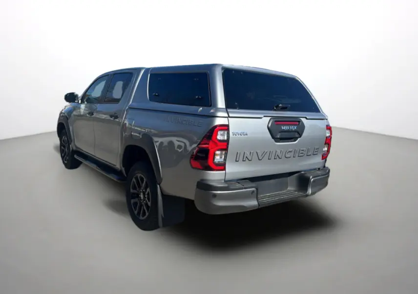 Toyota Hilux 4x4 gris acier en 3/4 arrière droit avec hardtop et logo Invincible visible sur la benne.