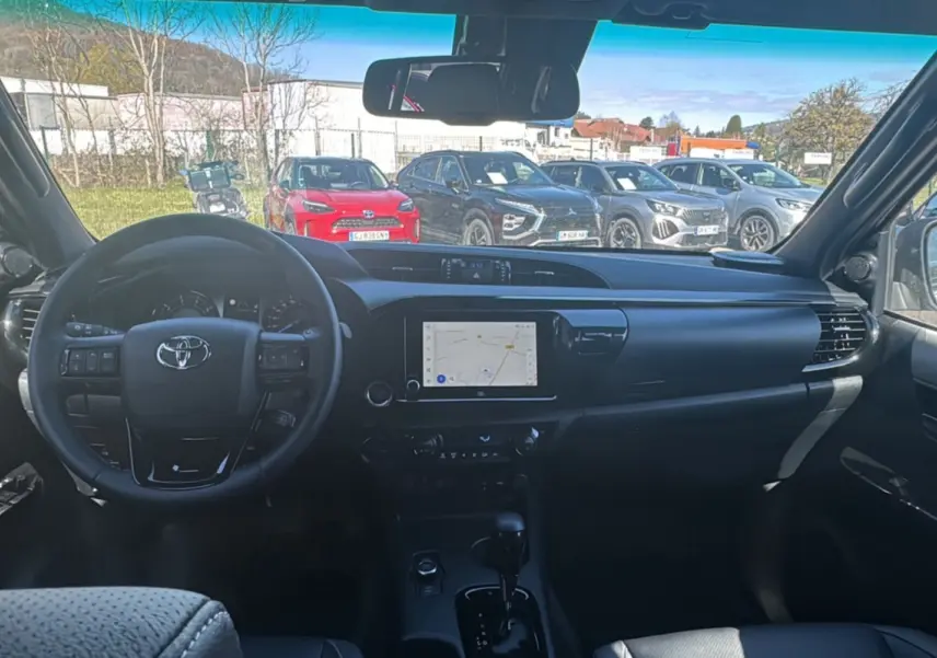 Vue intérieure du Toyota Hilux 2026 montrant le tableau de bord noir avec écran tactile et volant multifonctions.