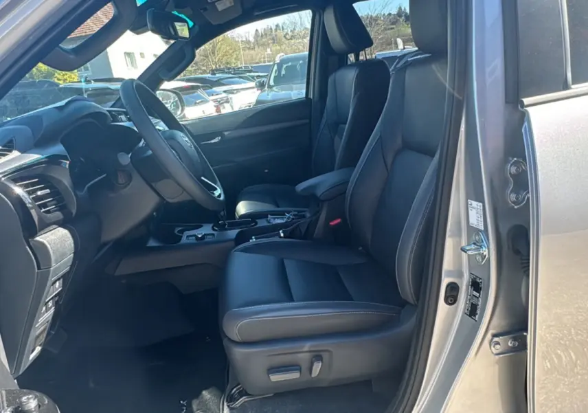Vue intérieure côté conducteur du Toyota Hilux 2026 gris acier, avec sièges cuir noirs et volant multifonctions.