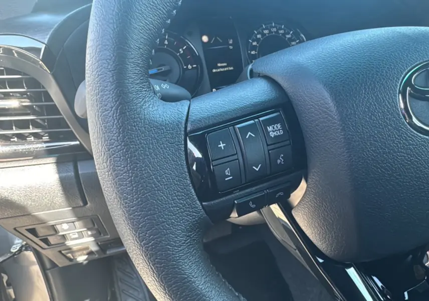 Gros plan sur le volant cuir multifonctions noir du Toyota Hilux 4x4 2026, avec commandes audio intégrées.