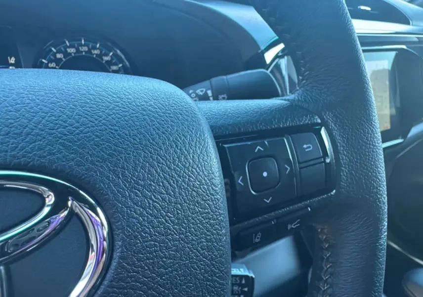 Gros plan sur le volant cuir multifonctions du Toyota Hilux 4x4 gris acier, avec tableau de bord et écran tactile visibles.