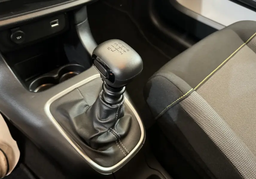Gros plan sur le levier de vitesse manuel en cuir noir et la console centrale d’une Citroën C3 gris foncé, siège tissu visible.