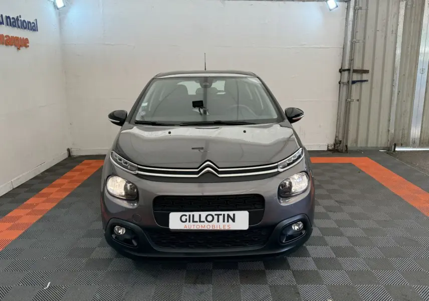 Citroën C3 gris foncé vue de face, avec feux allumés et calandre noire distinctive.
