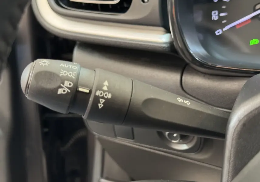 Gros plan sur la commande des phares et clignotants à gauche du volant cuir dans l’habitacle gris foncé du Citroën C3 2020.
