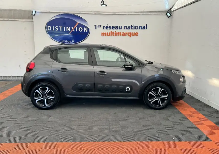 Vue de profil côté gauche d'une Citroën C3 gris foncé avec protections latérales noires et jantes alliage bicolores.