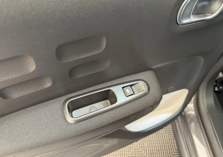 Gros plan sur la poignée intérieure et le bouton de verrouillage de la porte côté conducteur d'une Citroën C3 gris foncé.