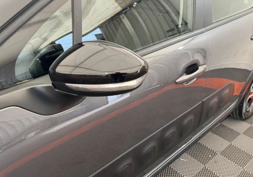 Gros plan sur le rétroviseur et la portière côté droit d'une Citroën C3 gris foncé avec protections latérales noires.