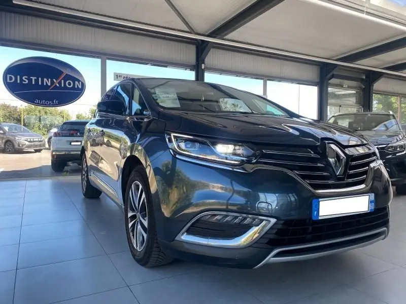 Renault Espace V gris vu en 3/4 avant droit, avec phares LED allumés et calandre chromée dans un showroom.