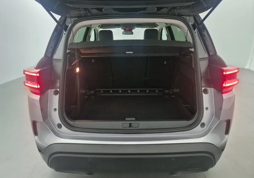 Coffre ouvert vu de l'arrière d'un Citroën C5 Aircross 2024 gris Artense avec feux arrière allumés dans un studio.