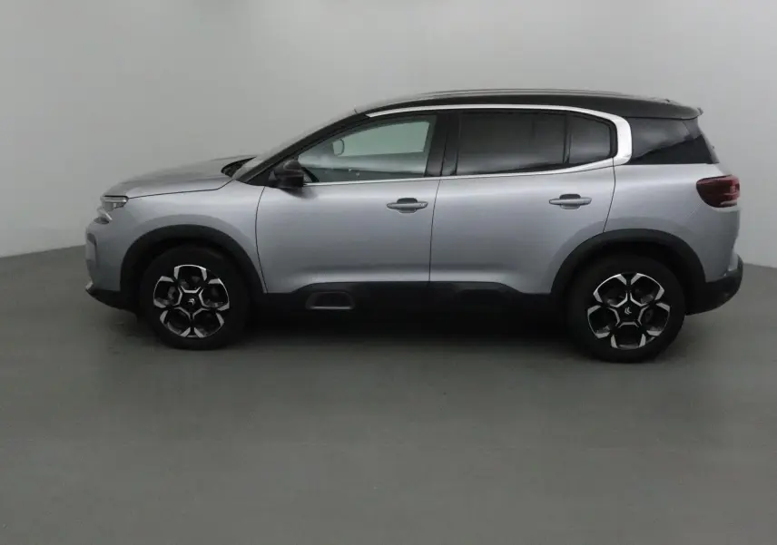 Profil côté gauche du Citroën C5 Aircross 2024 gris Artense avec toit noir et protections noires sur les bas de caisse.