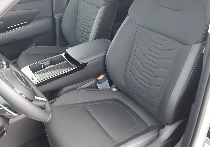 Vue intérieure côté conducteur du Hyundai Tucson 2025, sièges noirs en tissu avec détails en cuir et console centrale moderne.