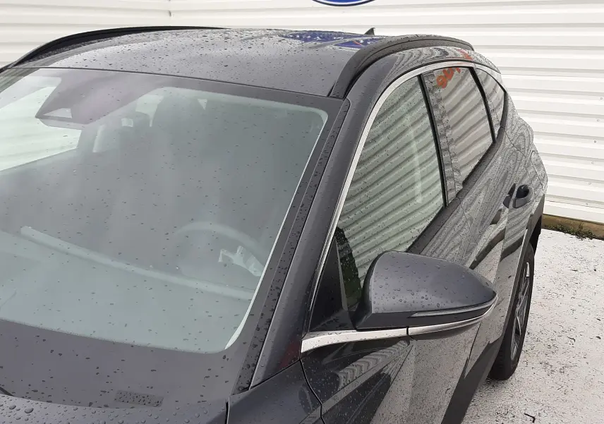 Vue 3/4 avant droit du Hyundai Tucson 2025 en gris Ecotronic, avec gouttes de pluie visibles sur la carrosserie.